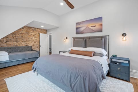 A stylish bedroom featuring a king-sized bed, brick wall, and blue sofa.