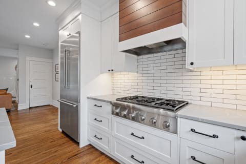 Interior view of a modern kitchen with a gas range, stainless steel refrigerator, and white cabinetry.