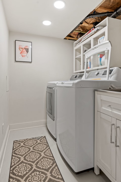 Modern laundry room with white appliances, shelving, and decorative art.