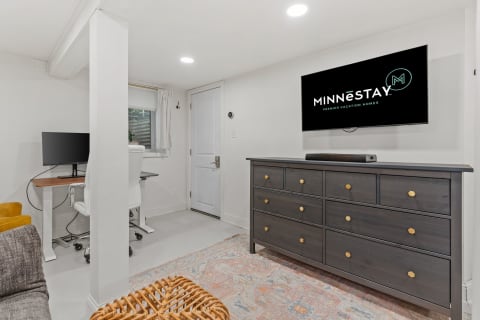 Interior view of a modern living area with a TV, dresser, desk, and sofa.
