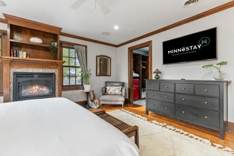 Warm and inviting bedroom featuring a fireplace, cozy armchair, and modern television.