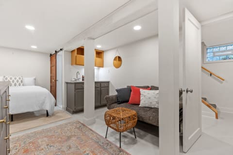 Modern basement studio with a bed, kitchenette, and seating area.