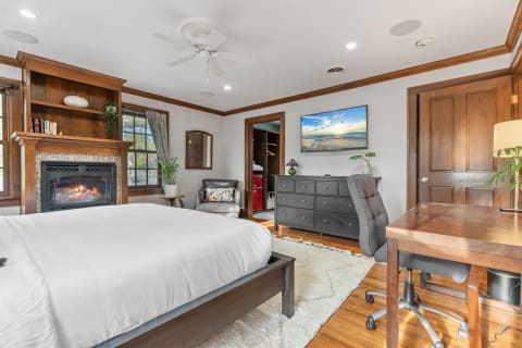 Inviting bedroom with wooden mantel fireplace, a comfortable armchair, and a flat-screen TV.