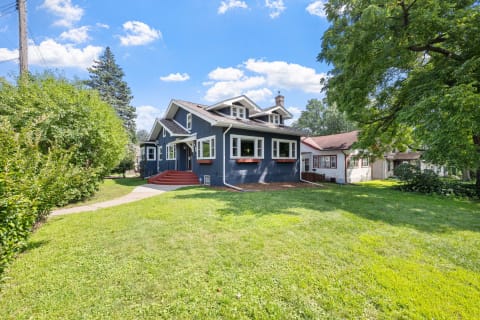 Exterior view of a charming blue two-story house with a lawn and pathway.