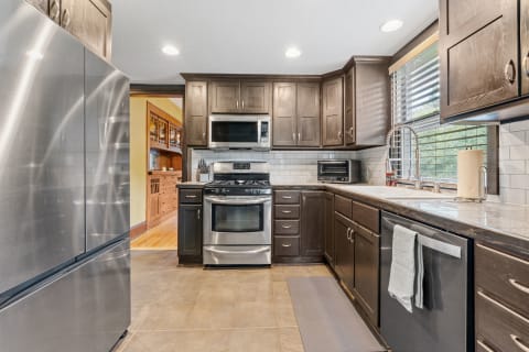A contemporary kitchen featuring dark wooden cabinets and stainless steel appliances, illuminated by natural light.