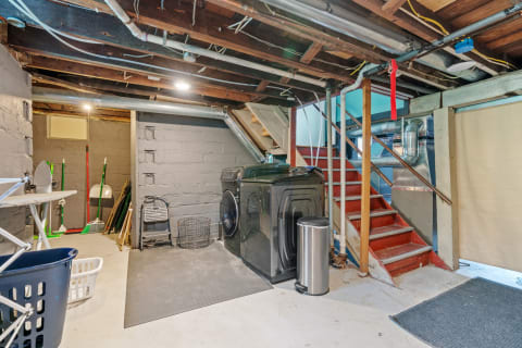 Basement laundry area with washing machine, ironing board, and cleaning tools.