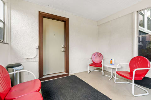 A porch with a door, red chairs, and sun protection products on a small table.