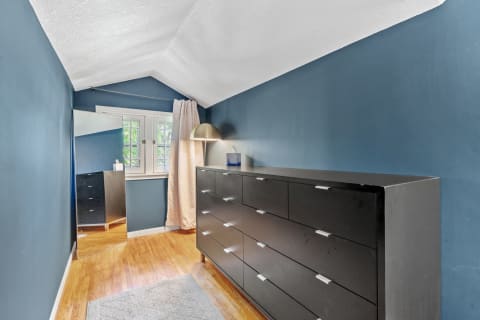 A room with sloped blue walls, a black dresser, and a full-length mirror.
