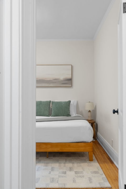 A cozy bedroom featuring a wooden bed with green cushions and a minimalist artwork above it.