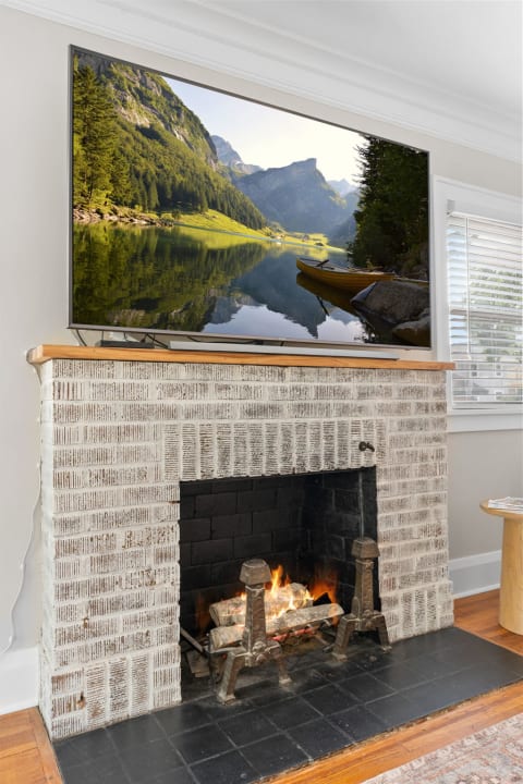 Living room with a flat-screen TV showing a landscape and a brick fireplace with a fire burning.