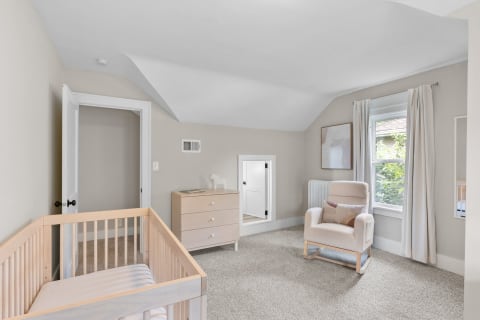 A cozy nursery featuring a crib, rocking chair, and dresser in soft neutral tones.