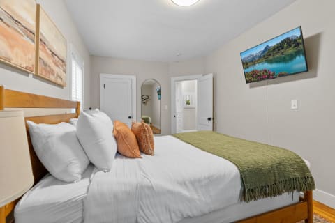 Cozy bedroom with a wooden bed, decorative pillows, and a mounted TV showing a landscape.