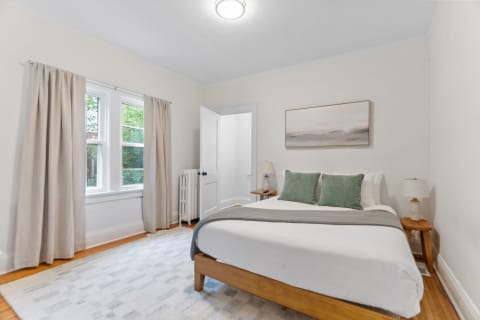 A softly decorated bedroom with a bed, nightstand, and window with curtains.