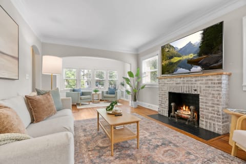 A bright living room with a fireplace, soft seating, and a TV displaying a mountain landscape.