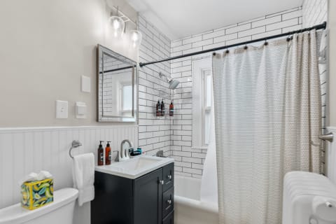 A modern bathroom with subway tiles, a black vanity, and a shower curtain.