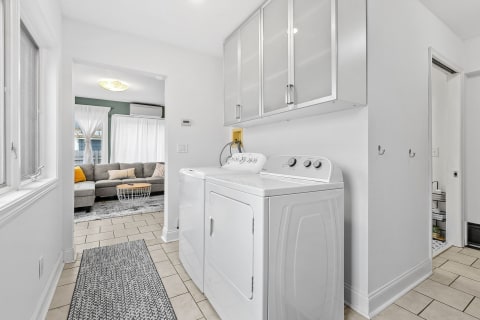 Modern laundry room with white appliances adjacent to a cozy living area.