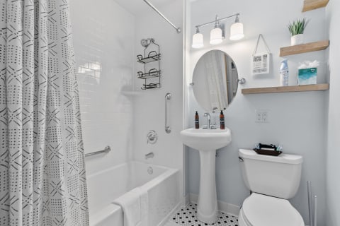 A small, modern bathroom featuring a bathtub, pedestal sink, and geometric shower curtain.