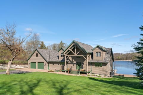 A lakeside house featuring earthy tones and modern architectural details with a clear blue sky in the background.