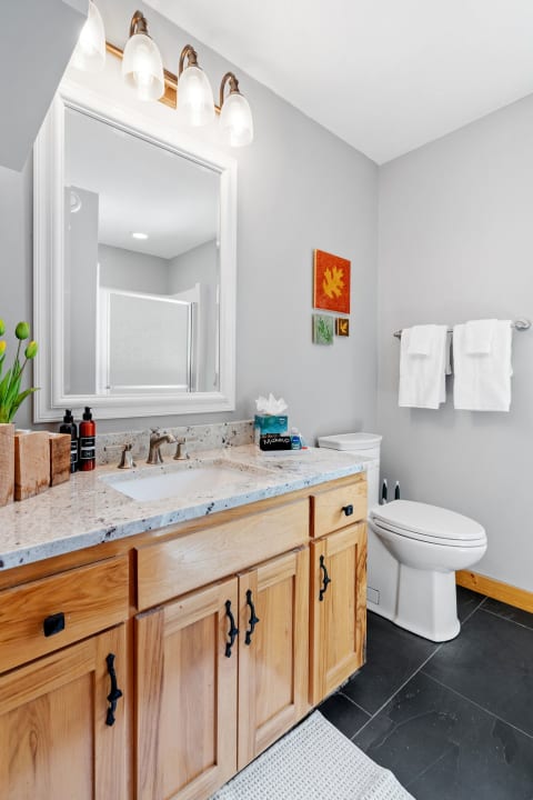 Modern bathroom featuring a light wood vanity, granite countertop, and colorful wall art.