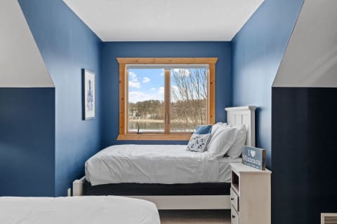 Bedroom with blue walls, a window showing a natural landscape, and white bedding.