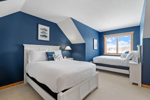 A cozy bedroom with a navy blue wall, featuring a main bed and a daybed, with a large window showing a snowy landscape outside.