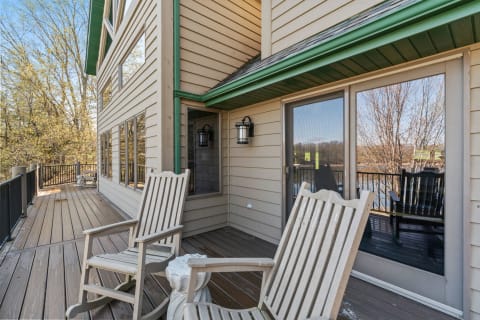 Outdoor deck with wooden rocking chairs and a view of trees.