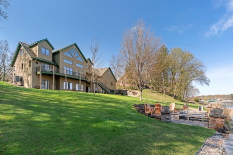 Lakeside home with a deck and outdoor seating area on a hillside.