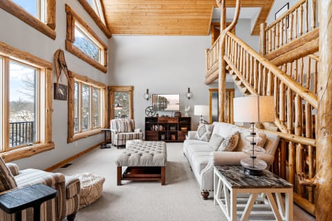 A spacious living room with wood beams, large windows, cozy seats, and rustic décor.