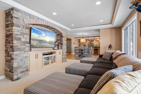 A spacious living room featuring a sectional sofa, a stone arch with a TV, and a dining area in the background.