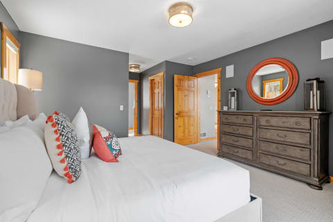 A cozy bedroom featuring a white bed, decorative pillows, gray walls, and wooden furniture.