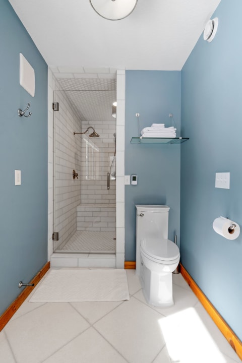 Modern bathroom with blue walls, white tile shower, and shelf of towels.