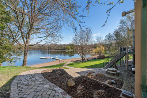Lakeside scene with a paved path, sandy shore, and a dock under a clear blue sky.