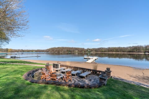 Lakeside view featuring a stone patio, chairs, and a wooden dock.