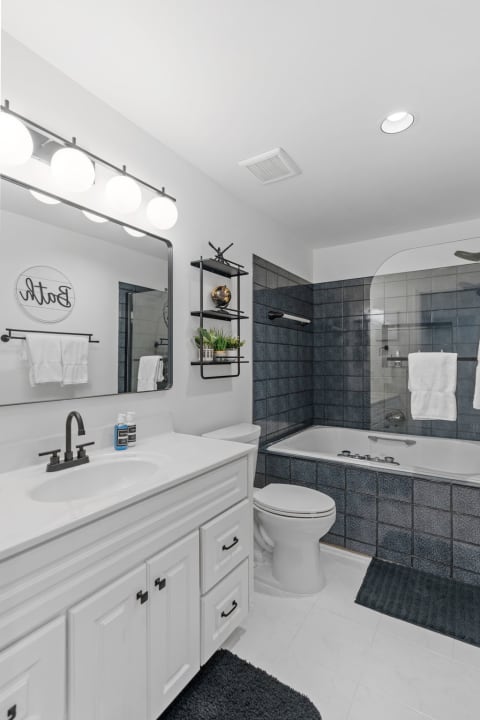 Modern bathroom with a white vanity, dark blue tiles, and a jetted tub.