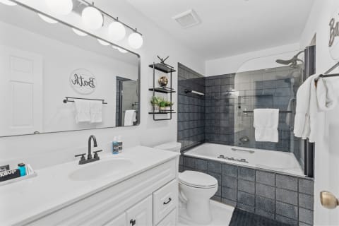 A contemporary bathroom with a white vanity, glass shower, and decorative shelving.