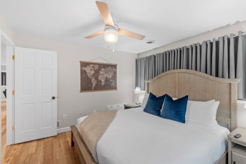 Cozy bedroom with a wooden bed frame, blue pillows, world map, and gray curtains.