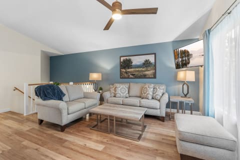 A comfortable living room with light gray sofas, a wooden coffee table, a blue wall, and a modern lamp.