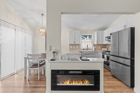 A modern kitchen featuring white cabinets, a dining nook, and an electric fireplace.