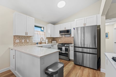 Modern kitchen featuring white cabinets and stainless steel appliances, with a decorative tile backsplash and natural light from a window.