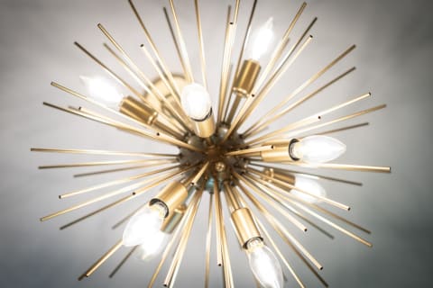 A contemporary chandelier designed in a starburst shape with gold rods and illuminated bulbs.