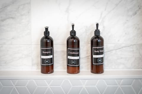 Three dark amber bottles labeled Shampoo, Conditioner, and Body Wash on a marble ledge.