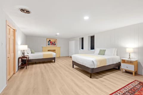 A spacious room with two beds, a lamp, a wardrobe, and a colorful painting on the wall.