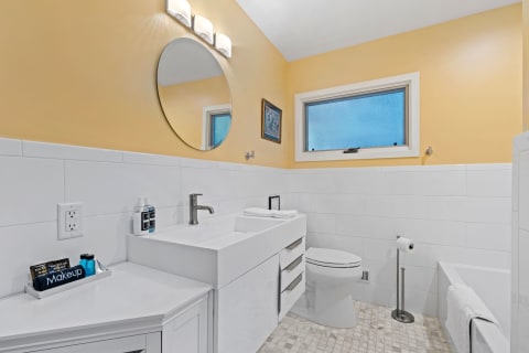 Contemporary bathroom featuring a yellow wall, a white vanity with a round mirror, and modern fixtures.