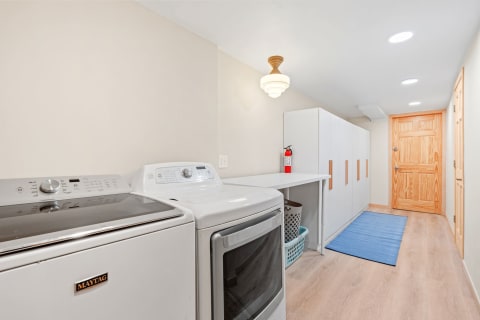 A bright and modern laundry room with Maytag washing machine and dryer, white cabinets and a blue mat on the floor.