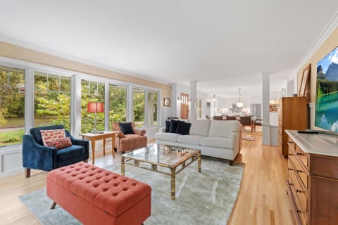 Inviting living room with large windows, cozy furniture, and a modern kitchen in the background.