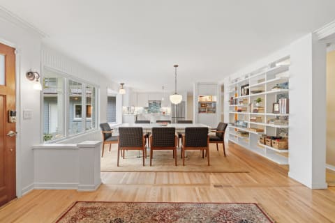Modern dining area with a large table, chairs, and bookshelf against white walls.