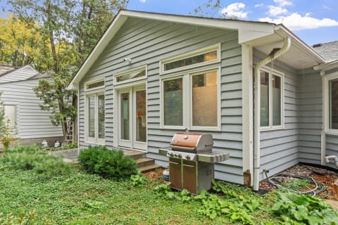 Exterior of a gray house with a barbecue grill surrounded by greenery.