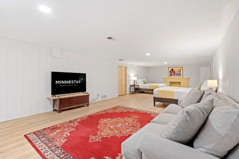 Spacious basement living area featuring a TV, sofa, and beds with soft lighting.