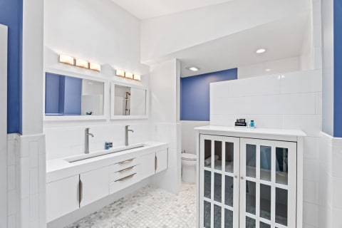 Modern bathroom with dual sinks, white cabinetry, and blue accent wall.