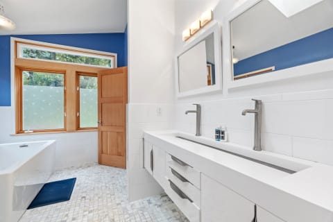 Modern bathroom with a blue wall, double sink vanity, and freestanding tub.